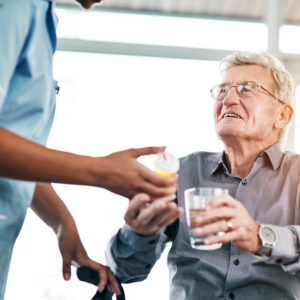 Nurse handing a glass of water to a smiling elderly man